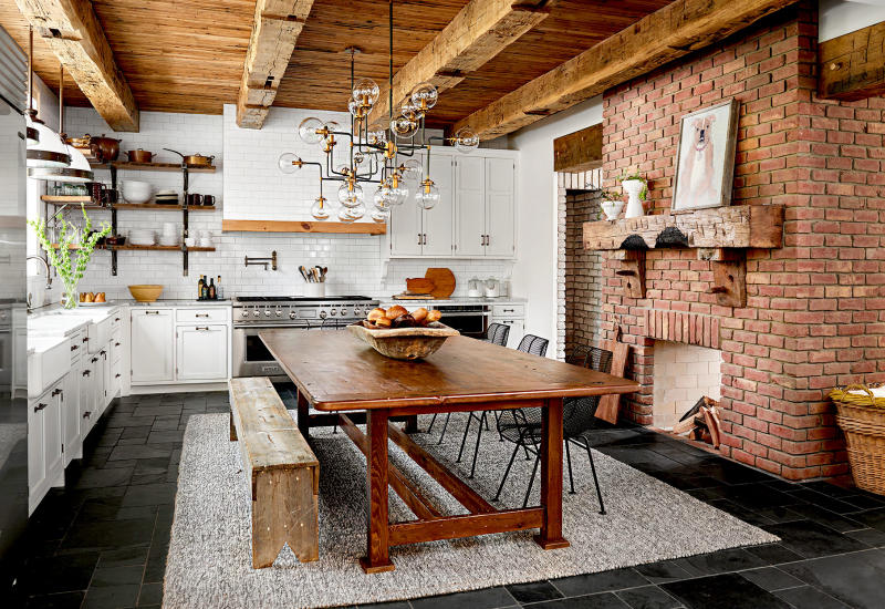 Đây là một mẫu nhà bếp kết hợp giữa nét hiện đại và mộc mạc. Yếu tố hiện đại đến từ hệ tủ trắng và các trang thiết bị làm bếp đời mới. Còn sự mộc mạc toát lên từ phần tường ốp gạch đỏ, trần gỗ và bàn gỗ 